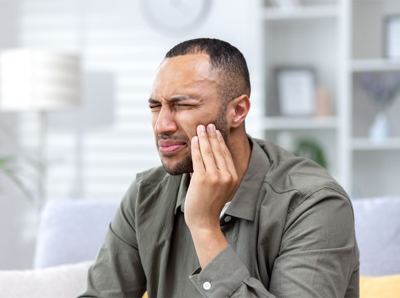 Man holding cheek in pain, illustrating dental emergency symptoms requiring urgent care.