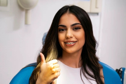 Smiling young woman with braces giving a thumbs-up while sitting in a dental chair