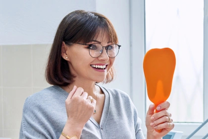 Happy woman admiring her smile in a tooth-shaped mirror after dental care
