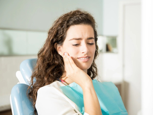 Woman sitting in a dentist’s chair, experiencing TMJ pain