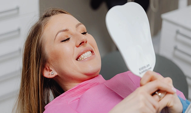 Woman smiling while seated in a dentist chair, looking at the mirror